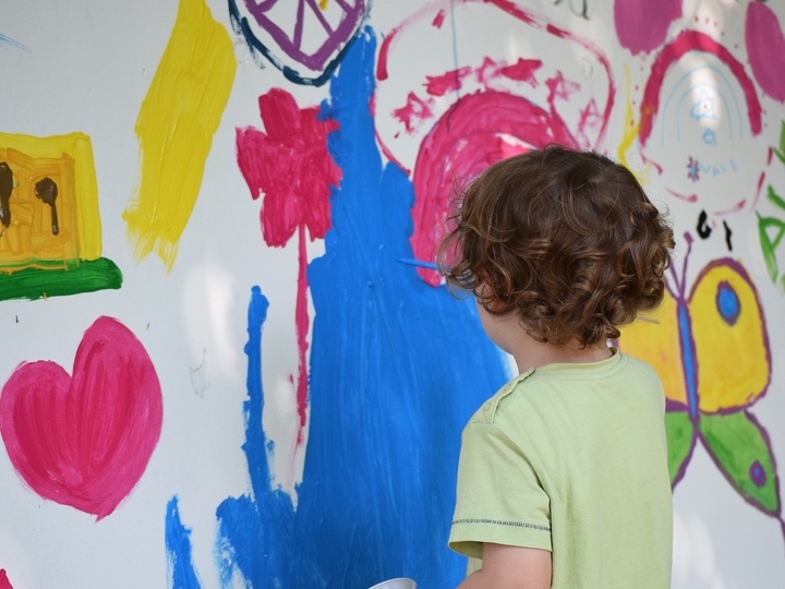 Kind malt mit Pinsel und Farbe an eine Wand. 